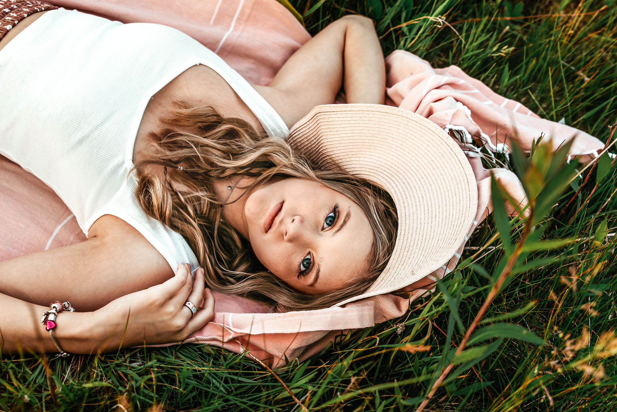 Dreamy outdoor portrait of woman lying in grass wearing white tank top.