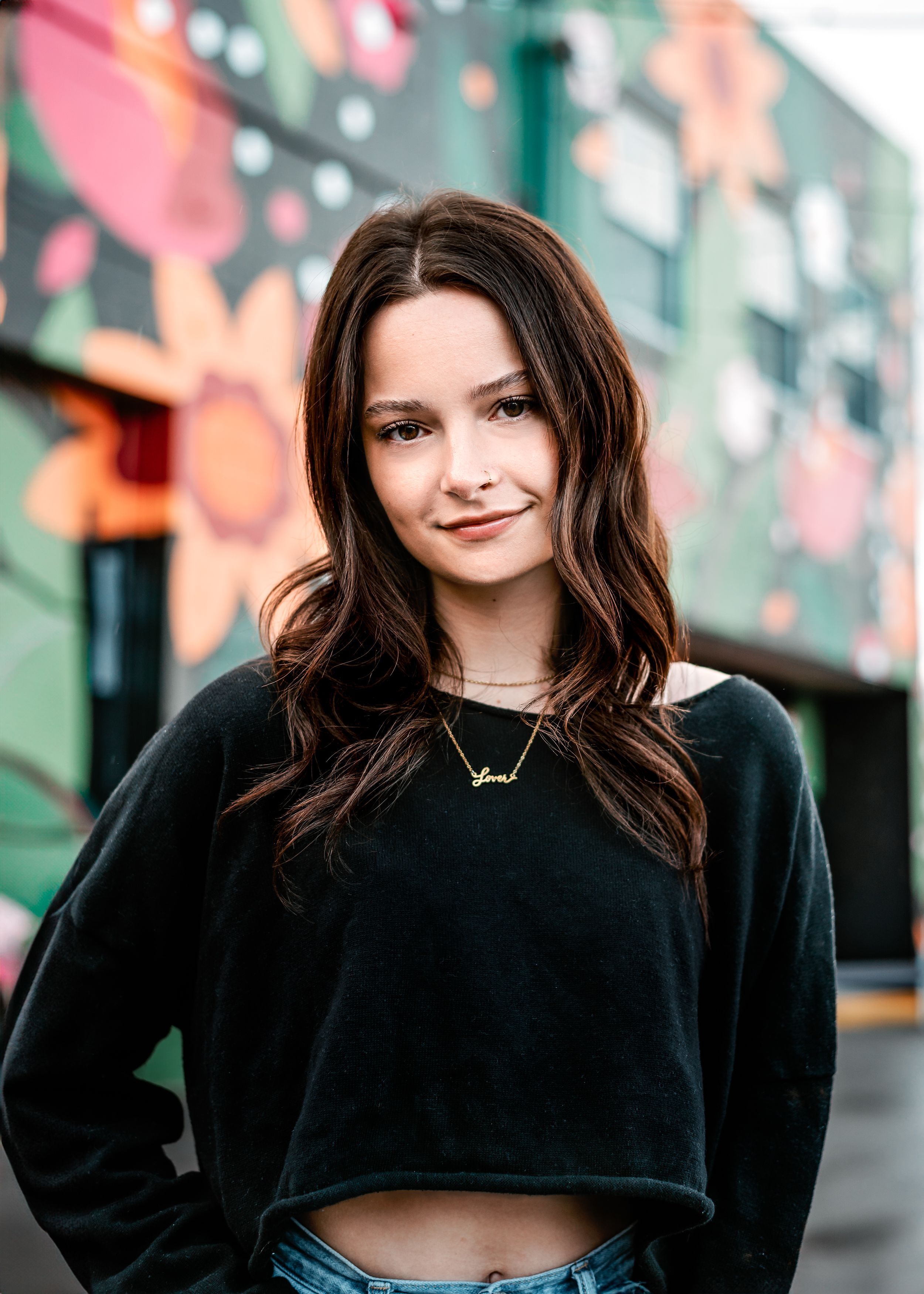 Portrait of a young person in black sweater against colorful urban wall art.