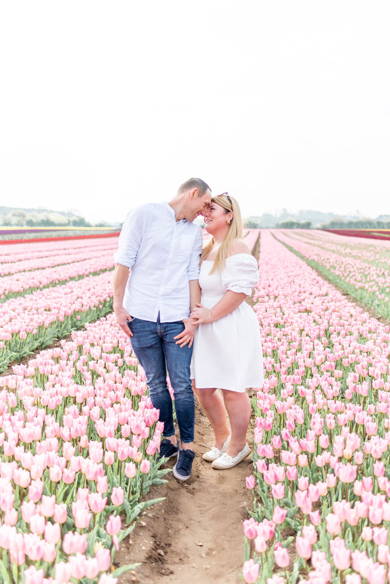 Couple in casual white outfits sharing an intimate moment in a field of pink tulips.