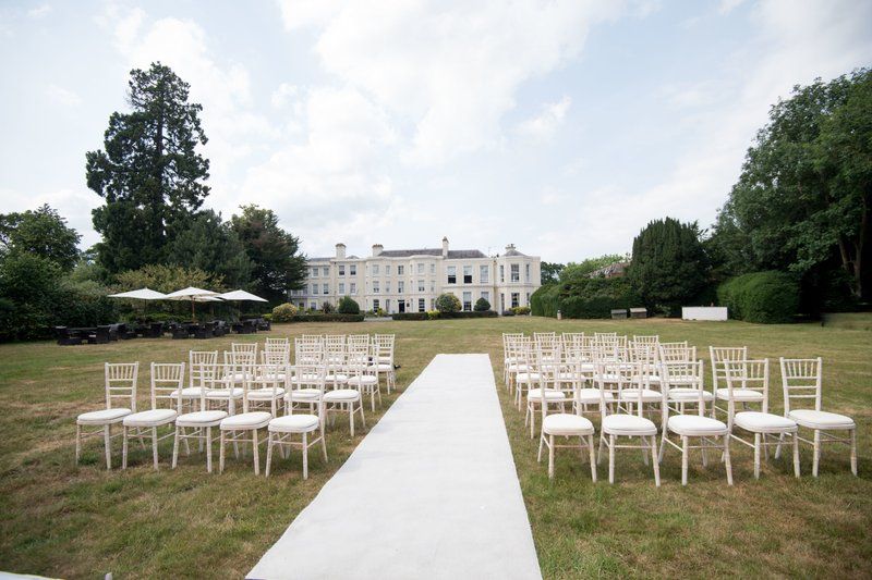 White chairs arranged in rows for an outdoor wedding ceremony with a grand mansion in the background.