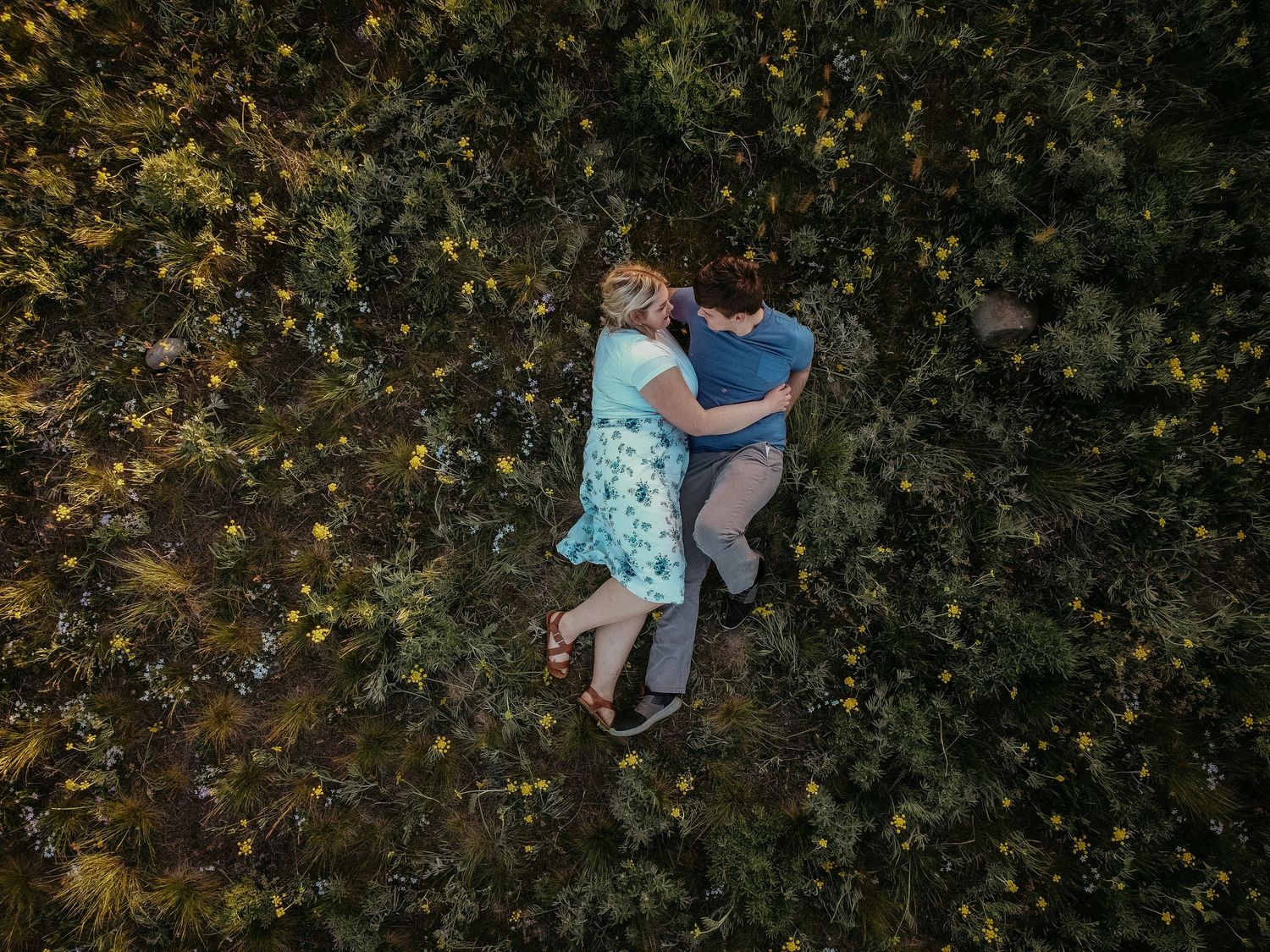 Couple lying in grass surrounded by autumn leaves viewed from above.