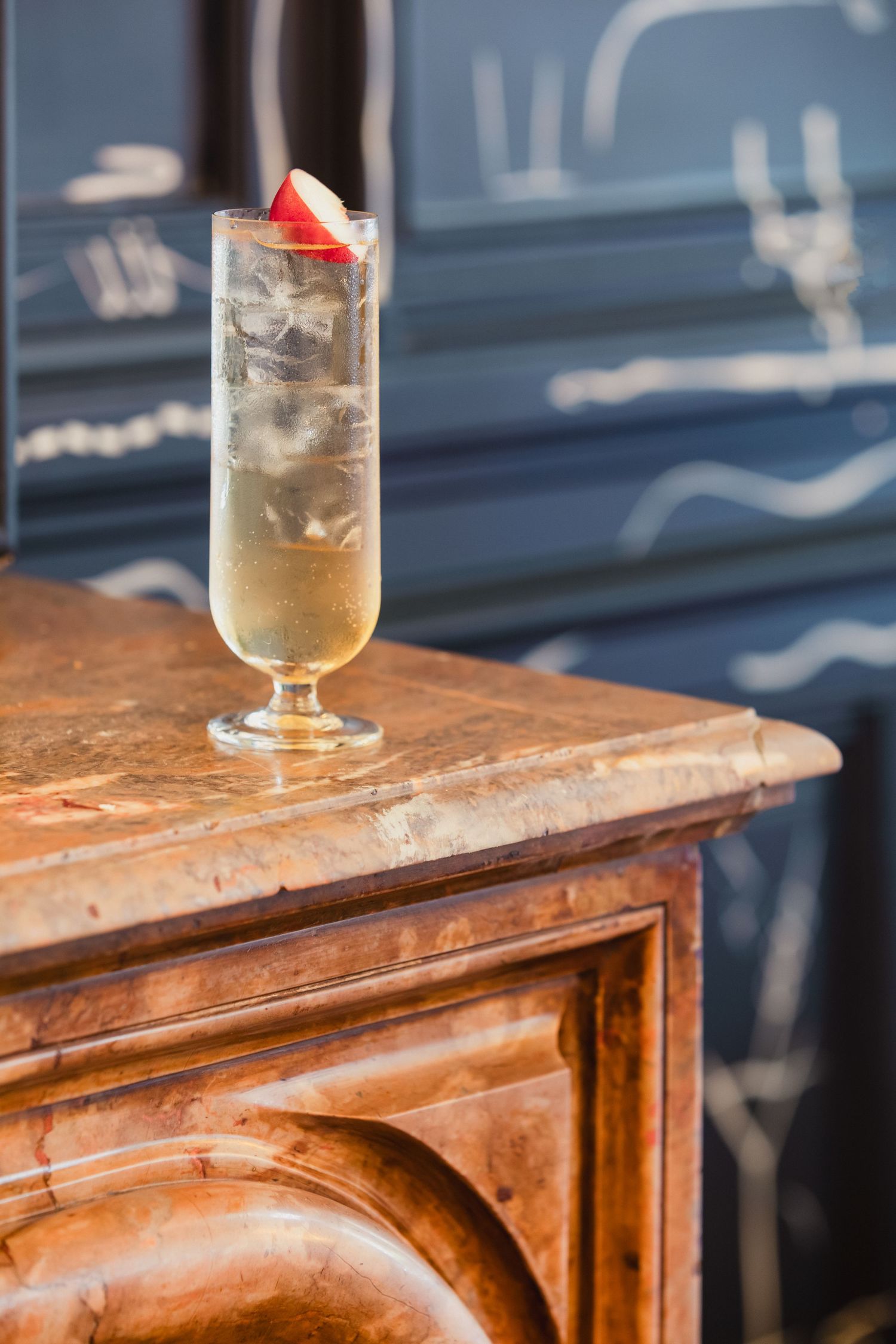 Tall cocktail glass with ice and strawberry garnish sitting on wooden antique furniture.