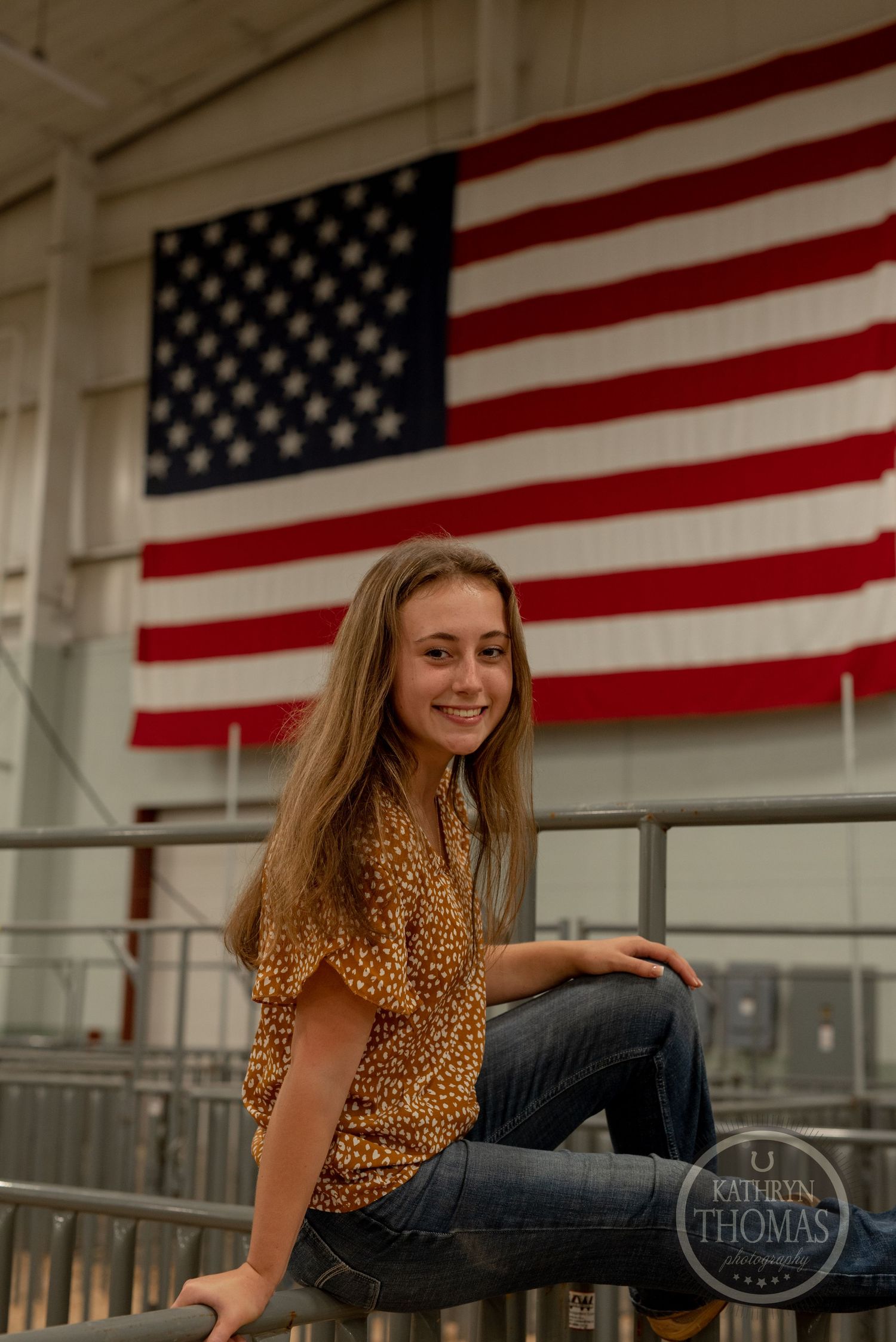 Casual portrait against American flag backdrop in agricultural facility wearing spotted shirt.