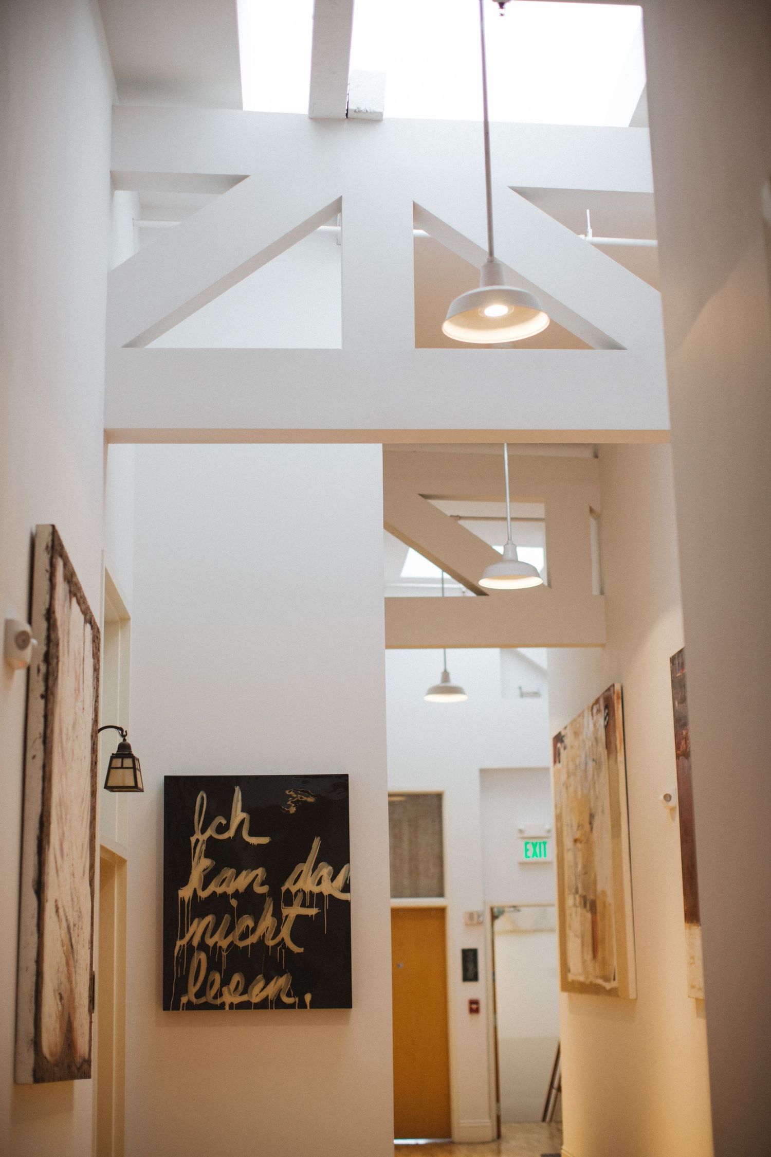 Modern white hallway interior with high ceilings, pendant lights and artistic wall decor.