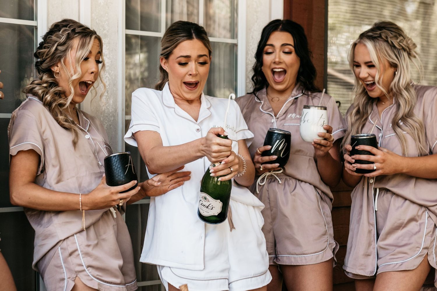 Wedding party in matching silk pajamas celebrating with champagne outdoors.