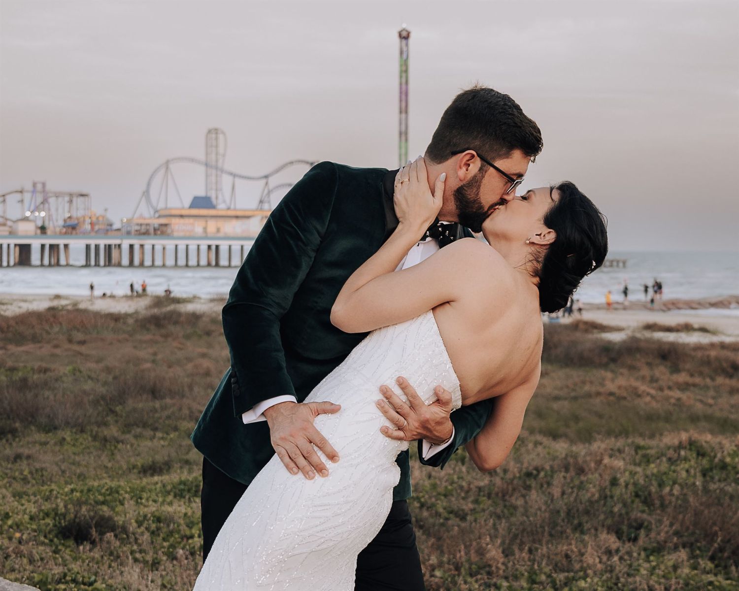 Romantic wedding couple embracing near a seaside pier at sunset.