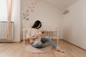 Nurturing moment in minimalist nursery with white crib and peach wall decor.