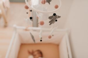 Baby mobile with gray plush toys and coral accents hanging above crib.