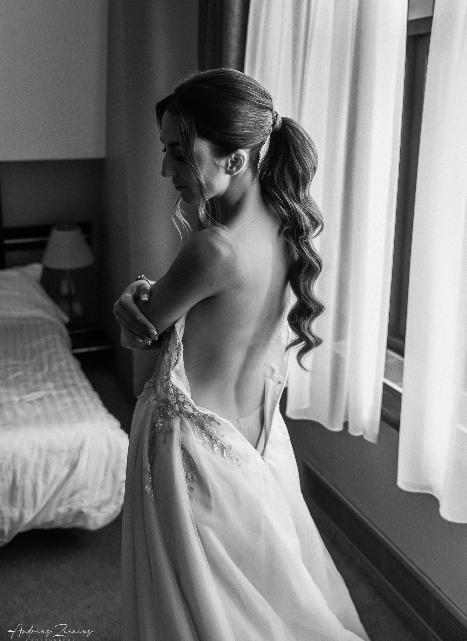 Elegant white wedding dress detail shot in black and white near a window.