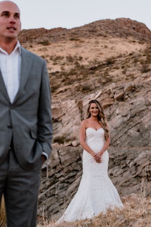 Couple in wedding attire pose against backdrop of rocky desert mountain landscape.