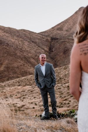 Wedding couple stand in intimate moment against desert mountain backdrop at sunset.
