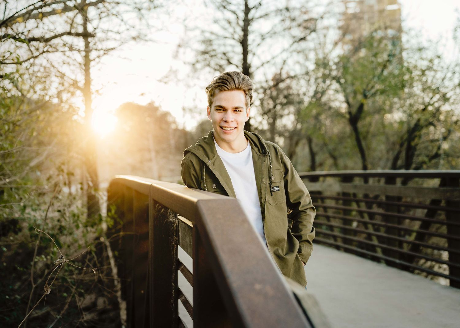 sunset behind a man standing on a bridge wearing an army green jacket at a park in houston, texas