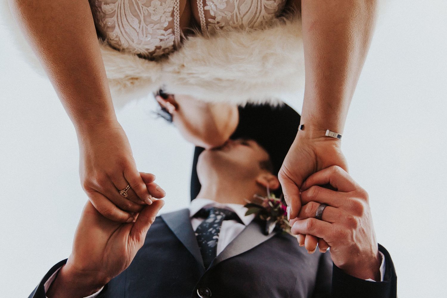 Bride and groom hold hands while kissing