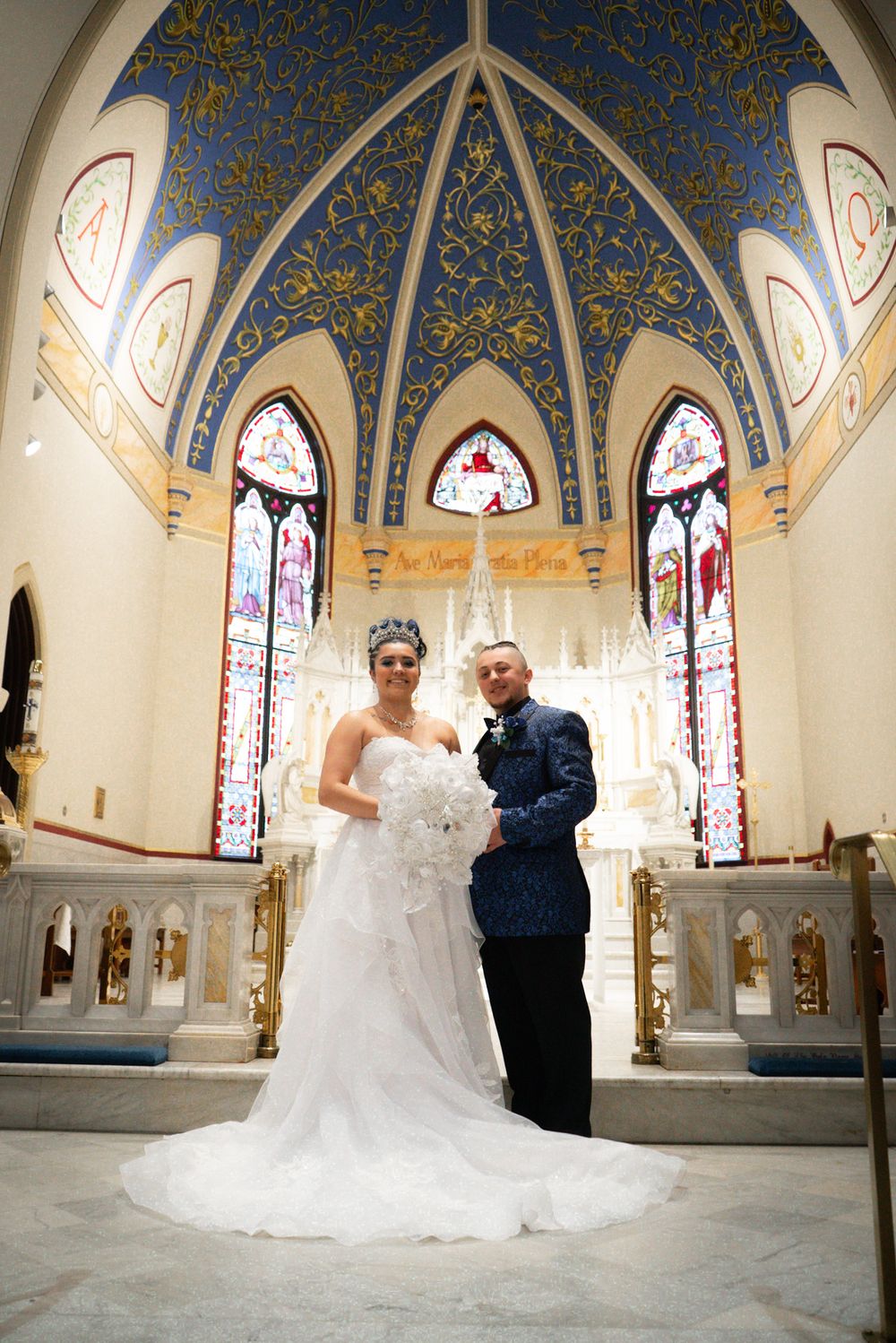 Wedding photo inside ornate church with blue and gold vaulted ceiling and stained glass windows.