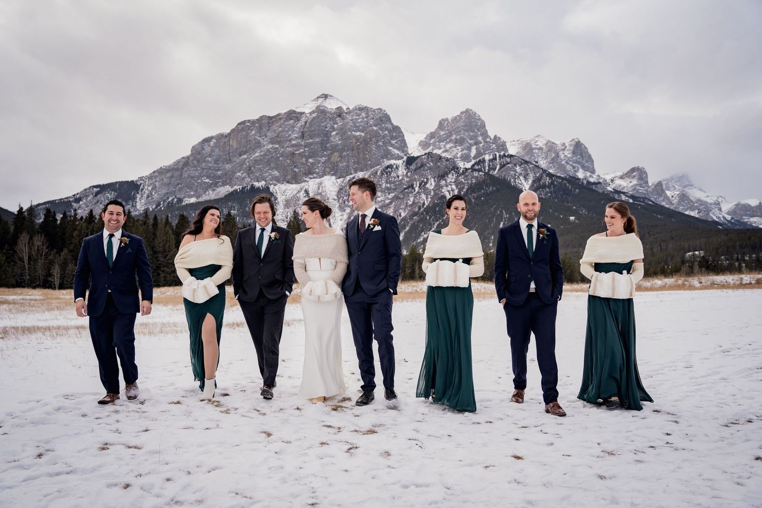 Wedding party standing in snow with dramatic mountain peaks in background.