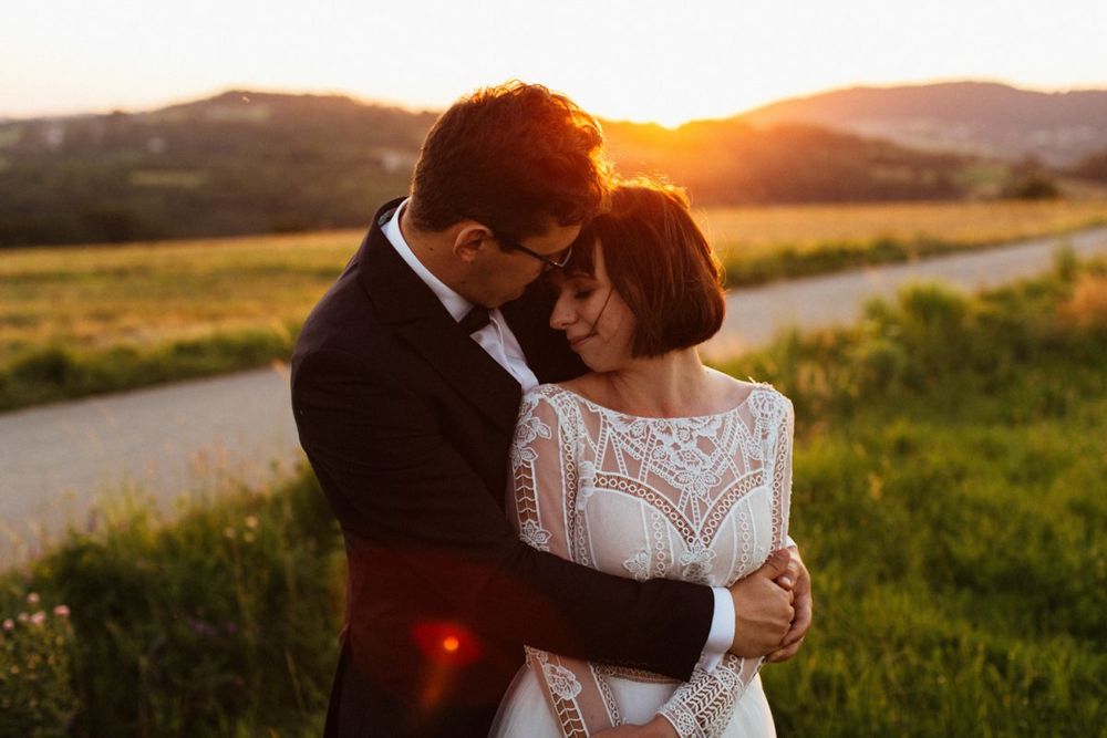 Bride and groom embracing tenderly at sunset with rolling hills in background.