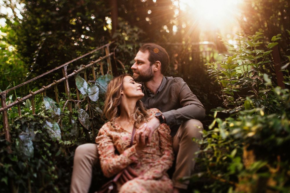 Romantic couple sitting together in lush green garden with golden sunlight filtering through trees.