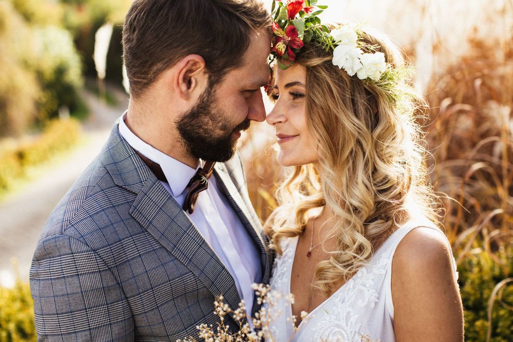 Bride with floral crown and groom in gray suit sharing intimate moment outdoors.