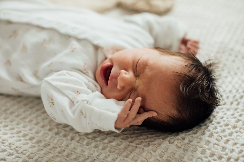 Newborn baby yawning while lying on soft blanket in peaceful nursery setting.