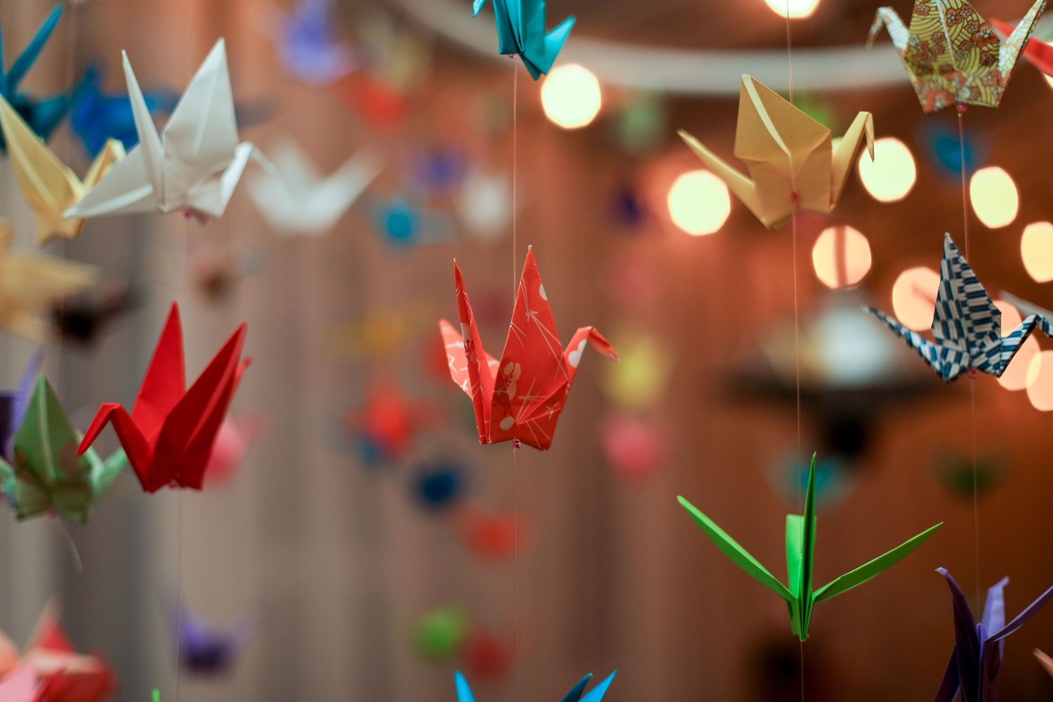 Colorful origami paper cranes hanging as wedding decorations with soft bokeh lights.