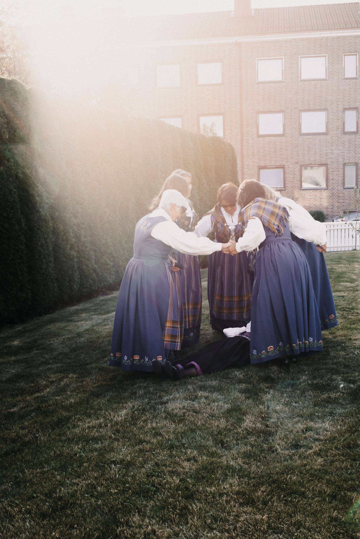 Group of people in traditional Norwegian folk costumes gathering in a circle during sunset.