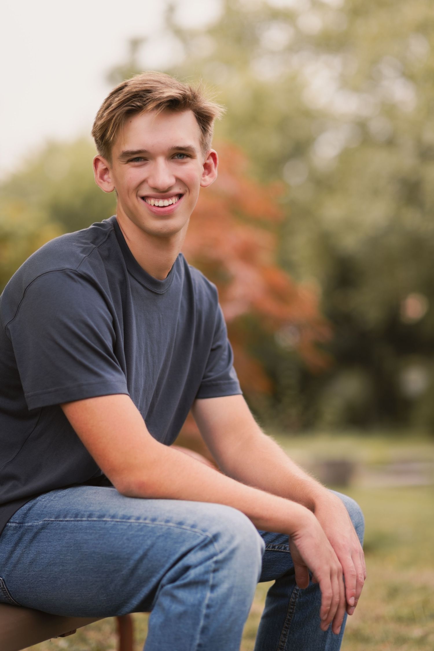 senior sitting on park bench shoulders away from camera looking at camera elbows resting on legs. cute smile