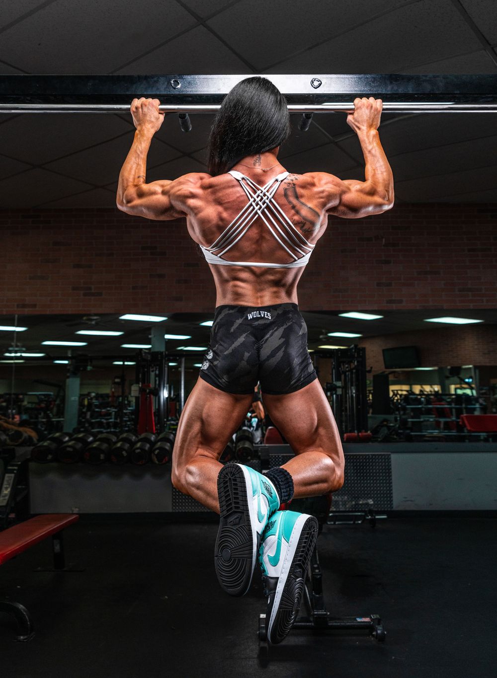 Athletic figure performing pull-up showing defined back muscles in gym setting.
