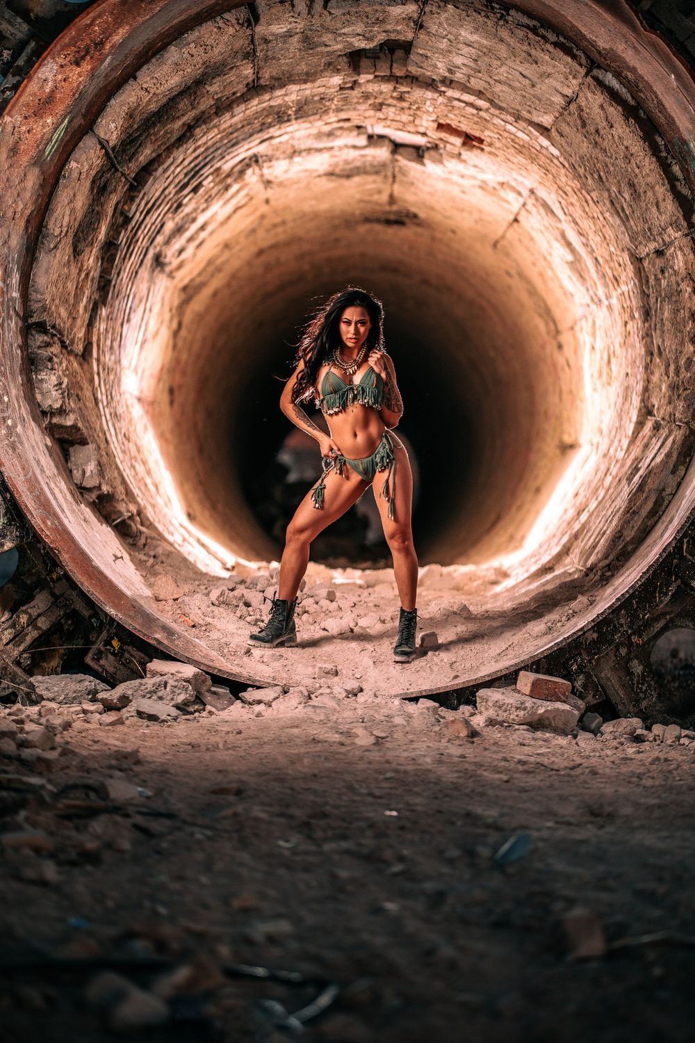Model poses dramatically in concrete tunnel with dramatic lighting.