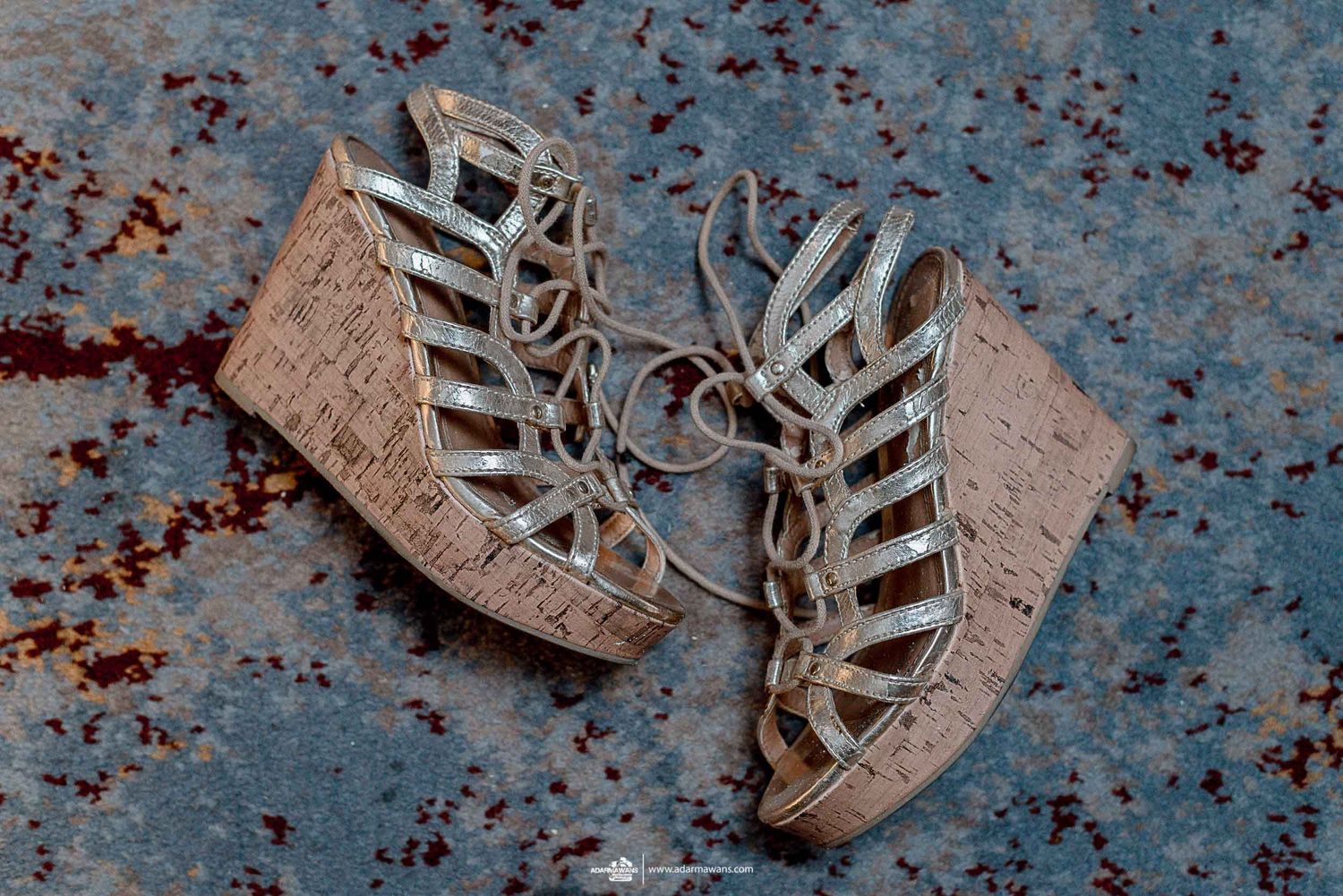 Strappy cork wedge sandals with woven details on a distressed blue surface.