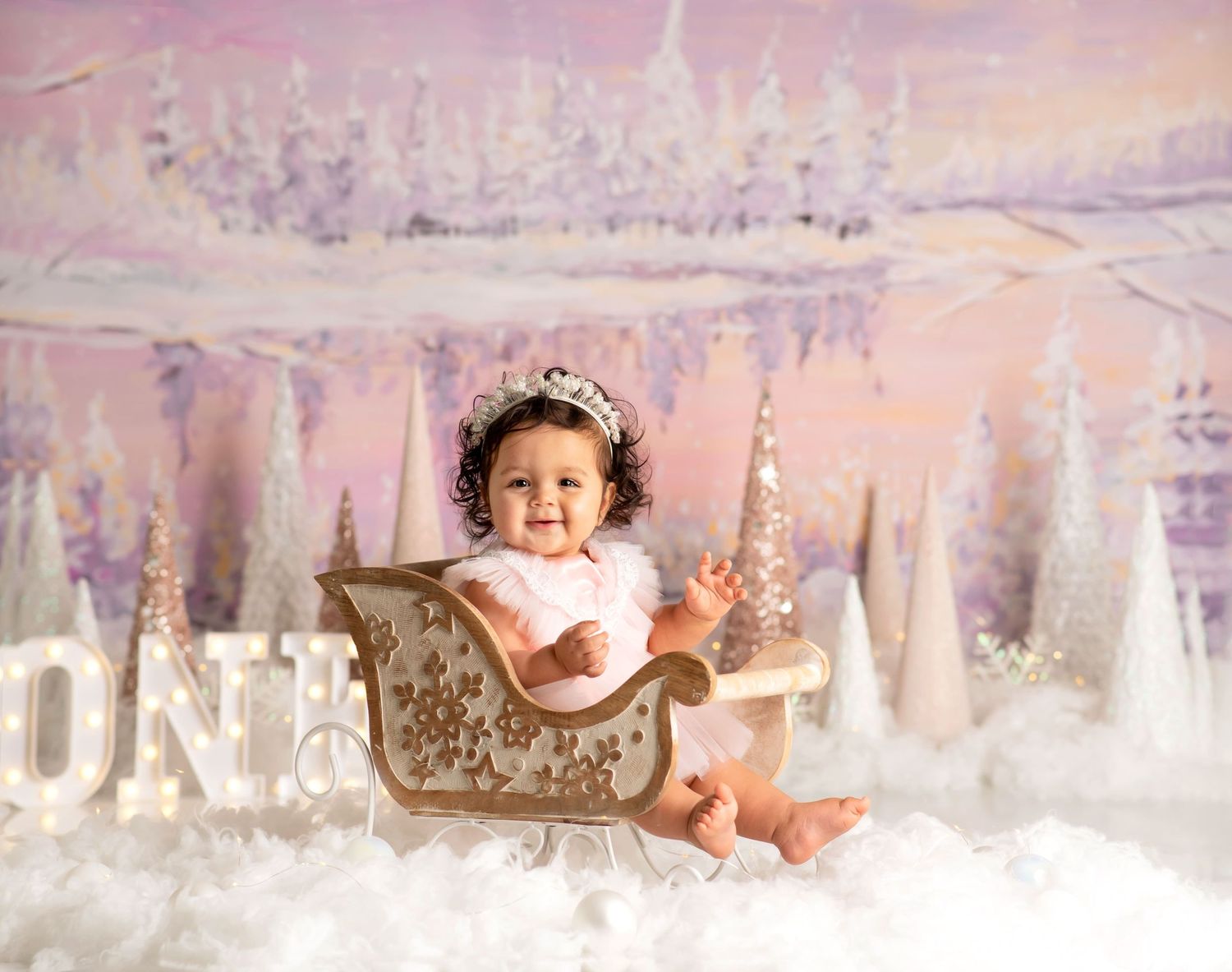 a girl smiles while sitting in a tiny sleigh for a winter onederland themed photoshoot
