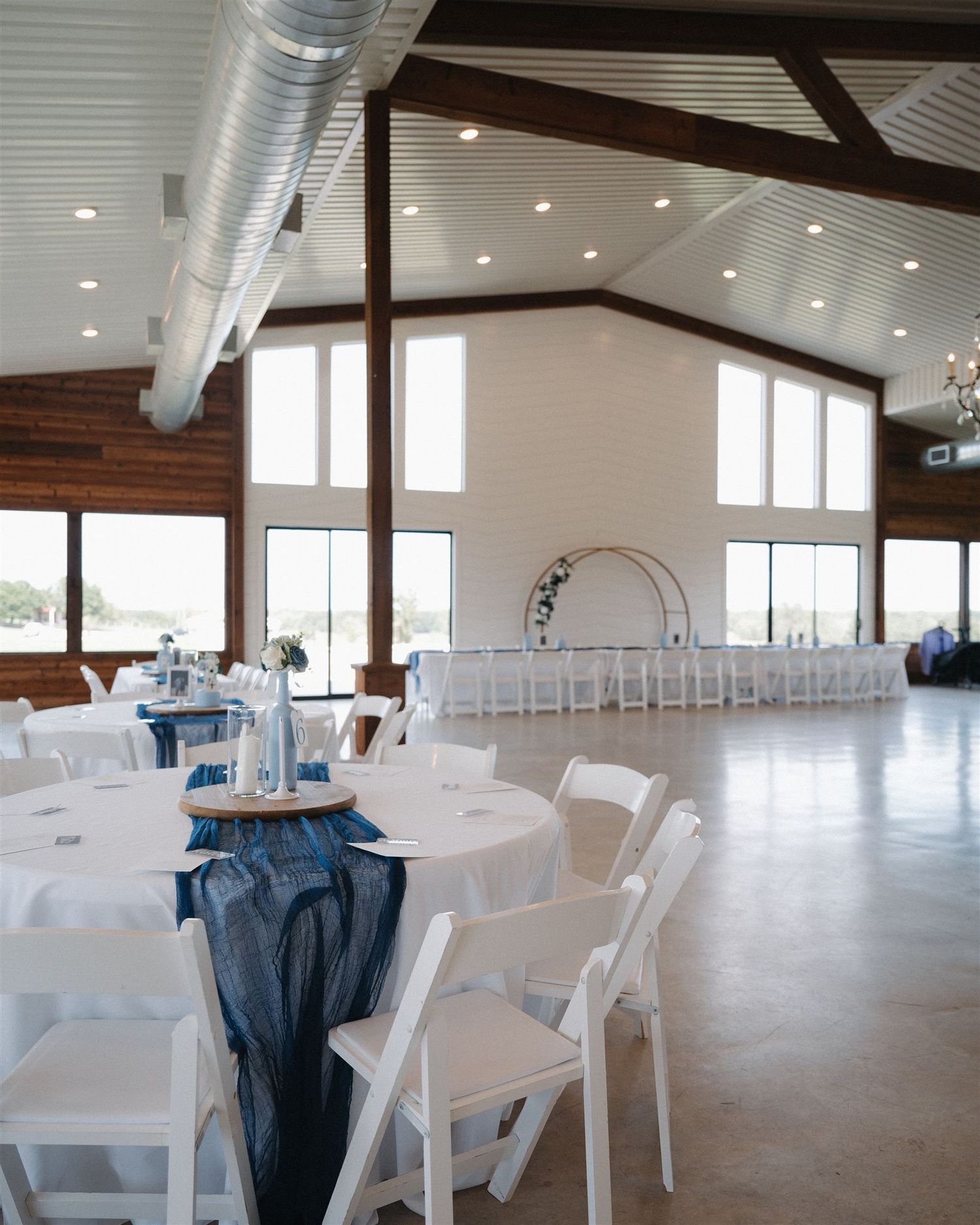 Wedding reception setup with white tables and blue accents in spacious modern venue.