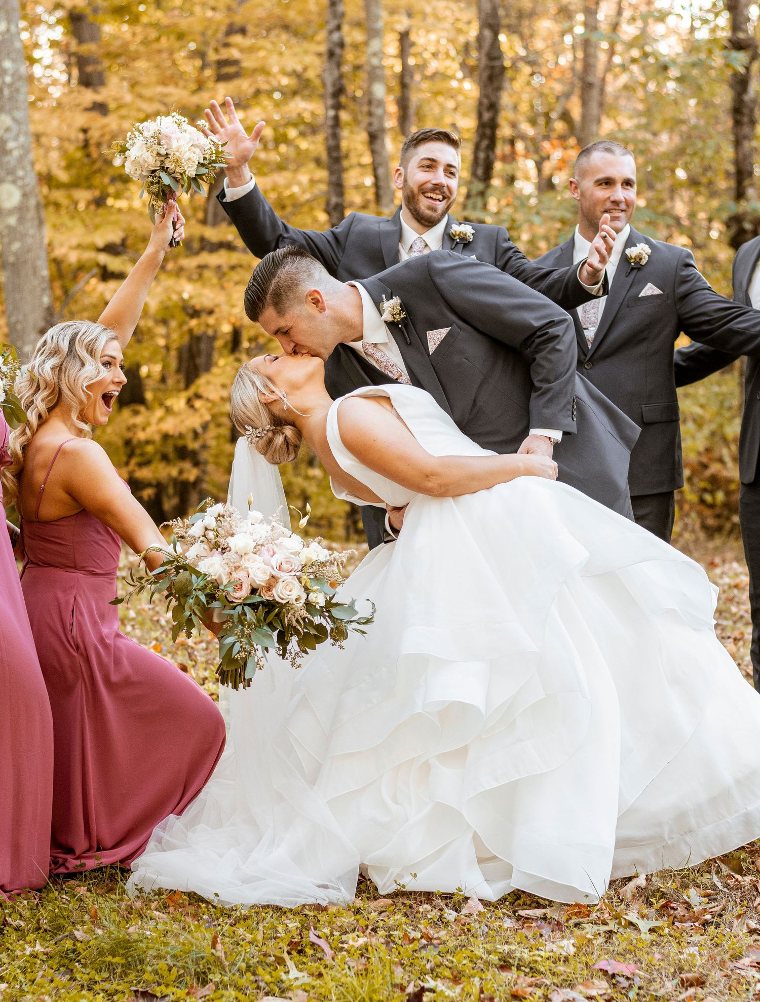 Wedding party celebrating with a dramatic dip pose in an autumn forest setting.