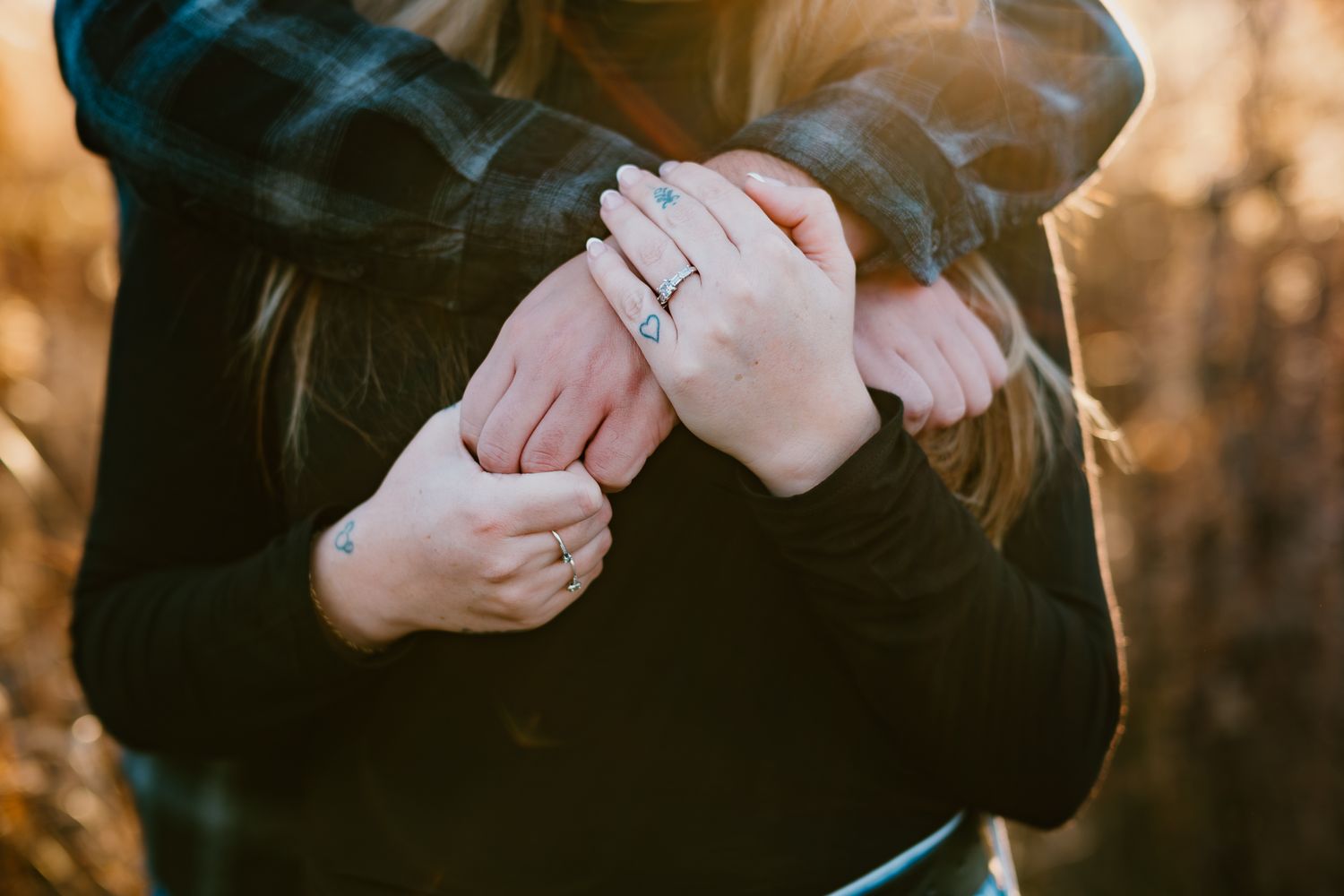 Close-up of hands showing off an engagement ring against a dark winter coat.