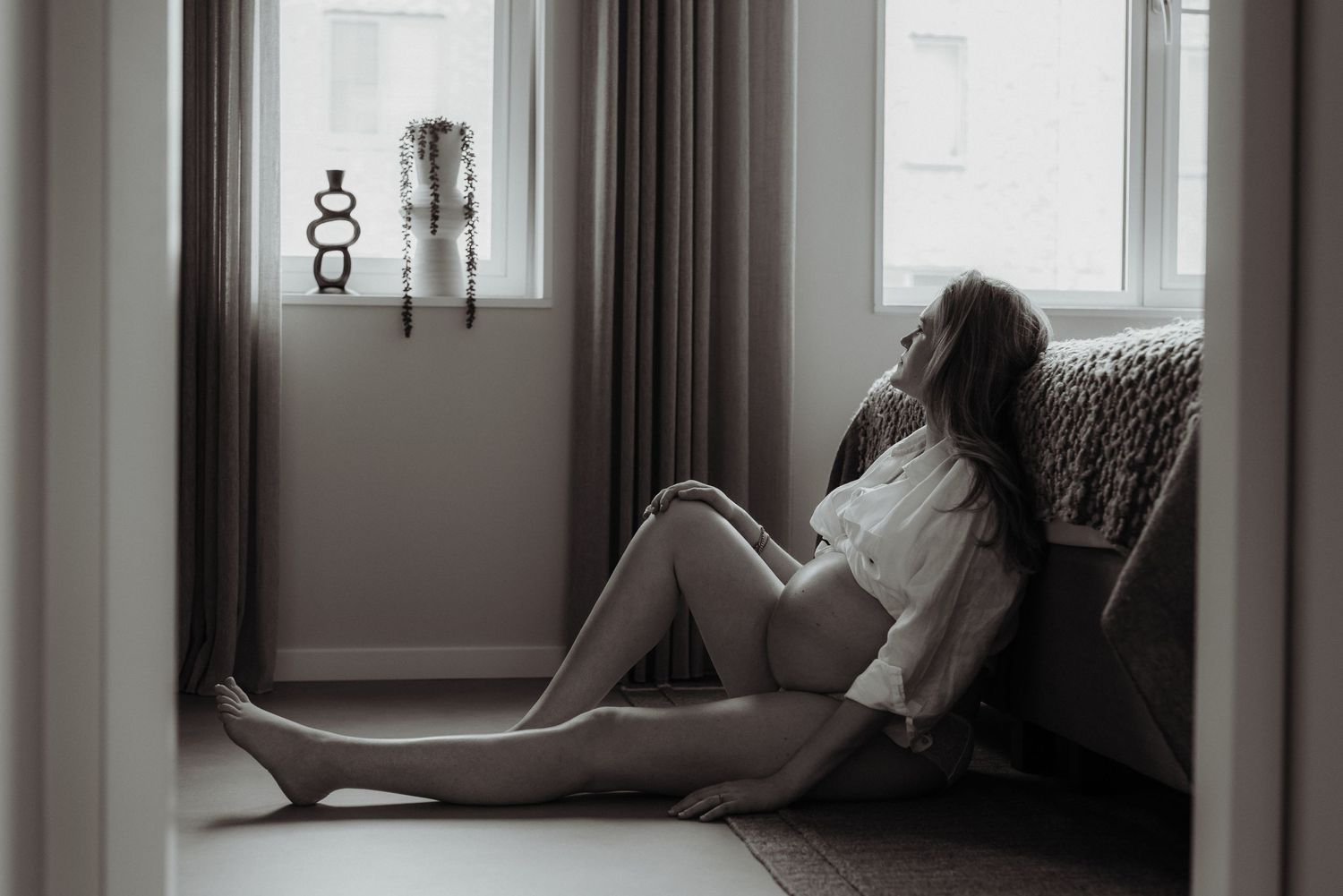 Moody maternity portrait of woman lounging in window light.