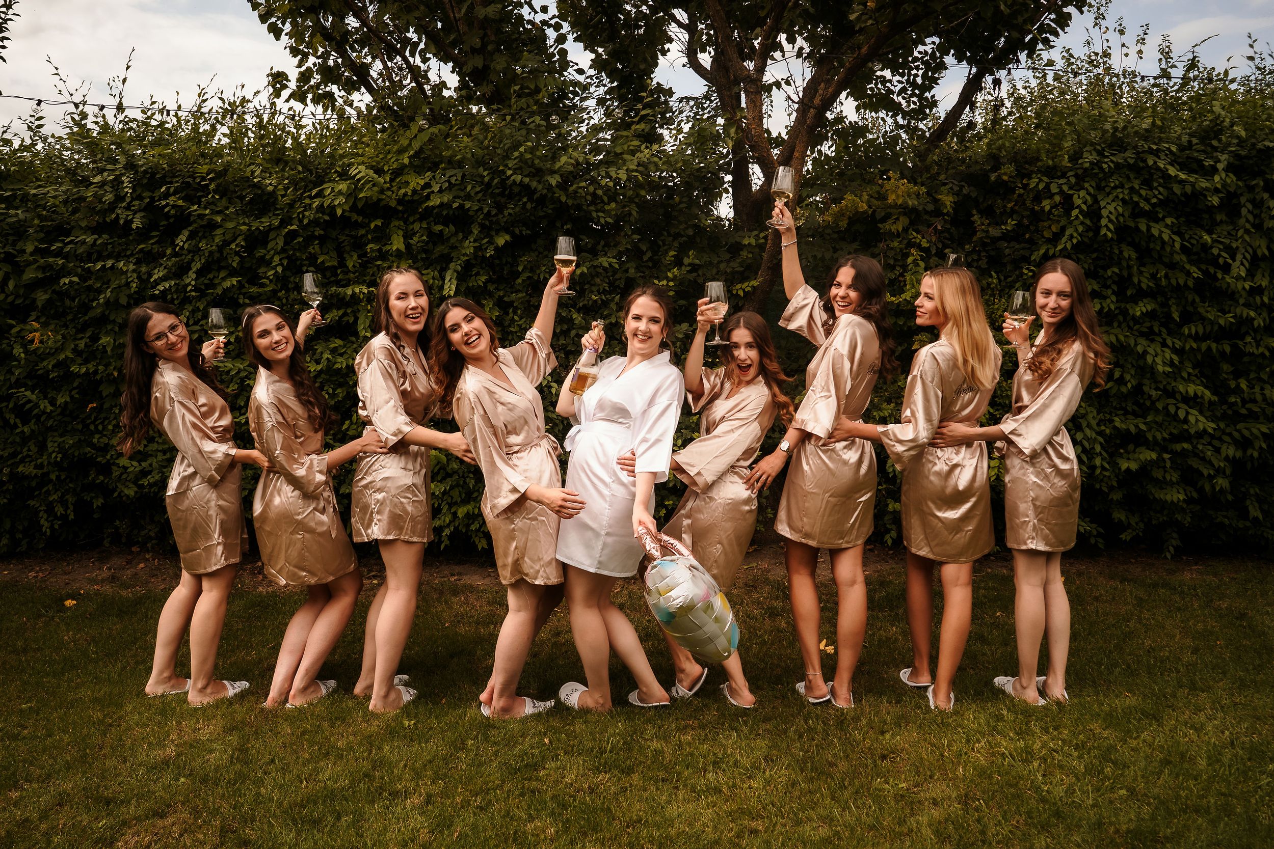 Wedding party in champagne colored robes posing together on grass.