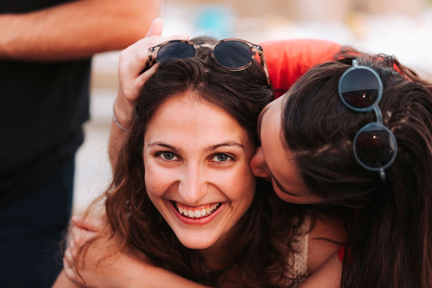 Close-up of joyful moment between friends with sunglasses outdoors.