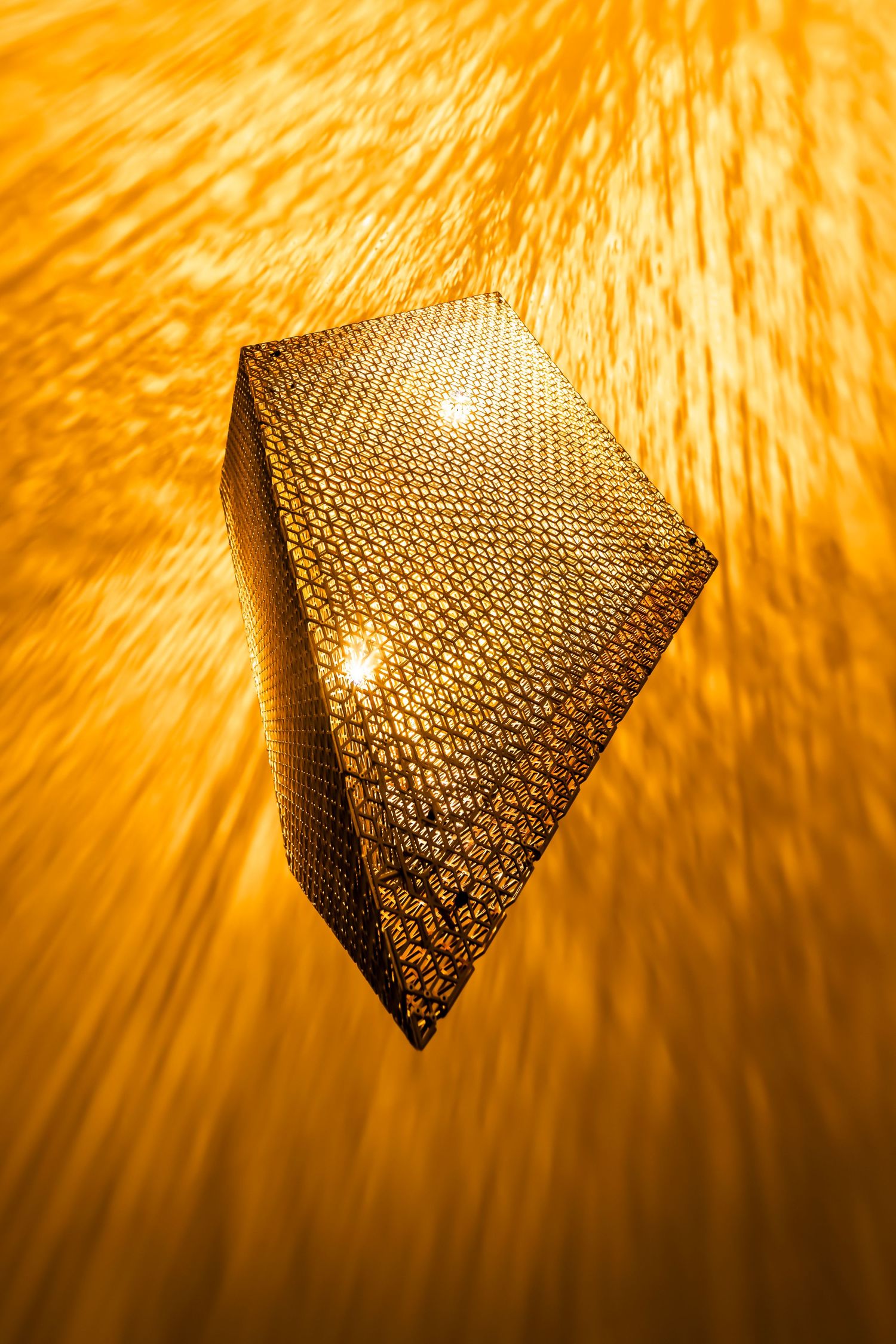 Geometric light fixture creating starburst pattern of warm orange light against wall.