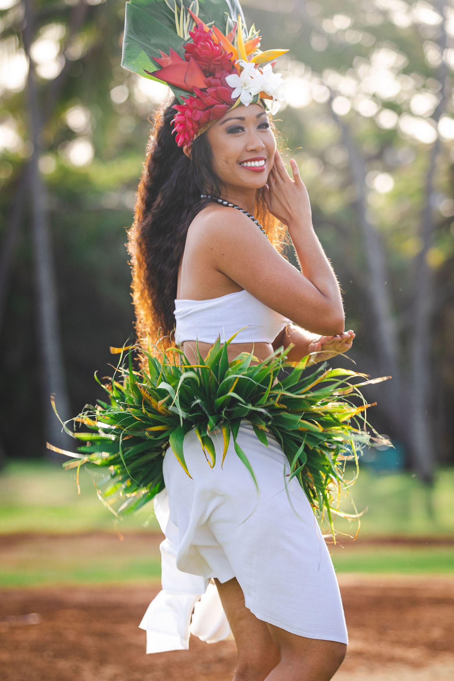 Polynesian dancer in traditional costume smiles while performing in tropical setting.