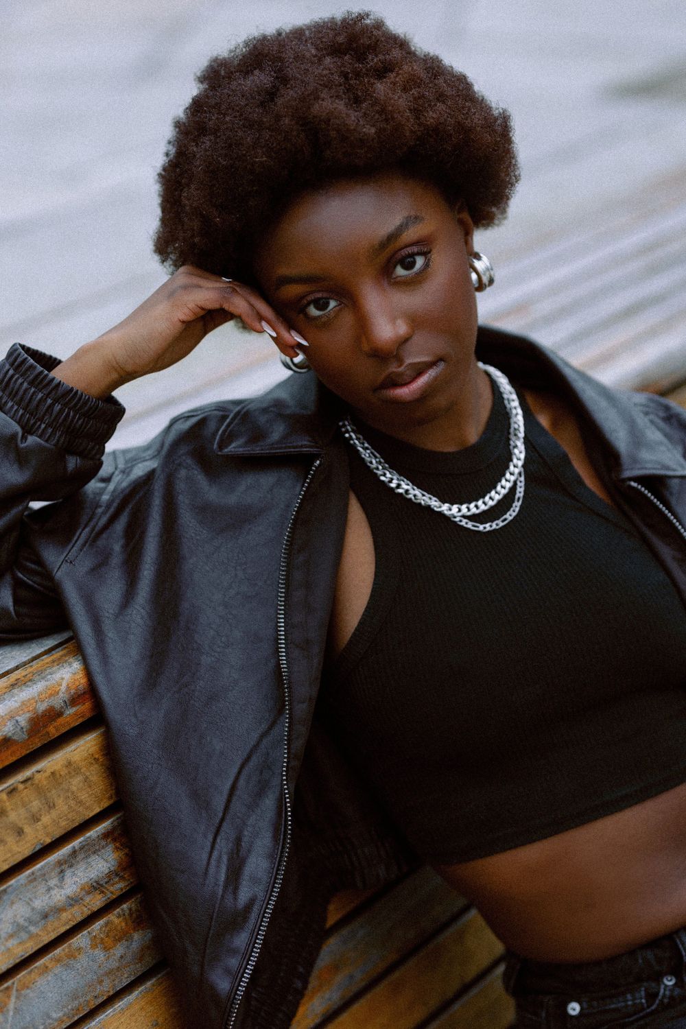 Stylish portrait series featuring leather jacket and chain necklace on wooden bench.