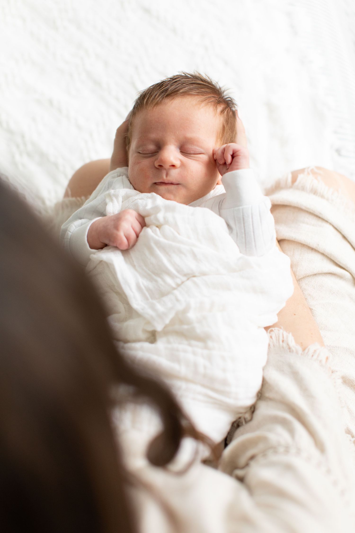 Peacefully sleeping newborn baby swaddled in white against soft bedding.