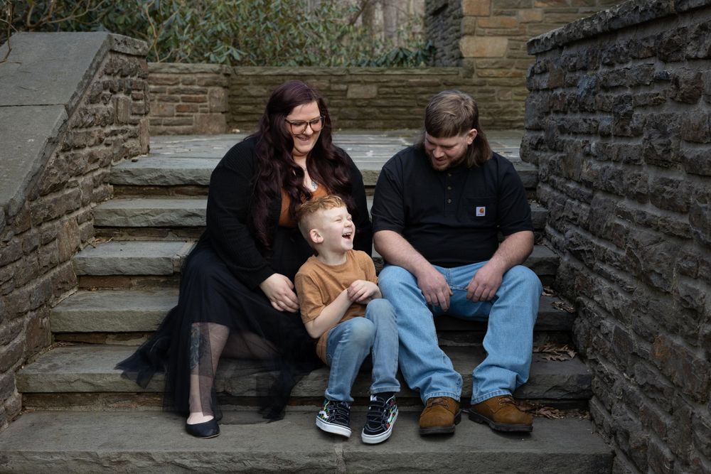 A family sits together on stone steps against a historic building wall.