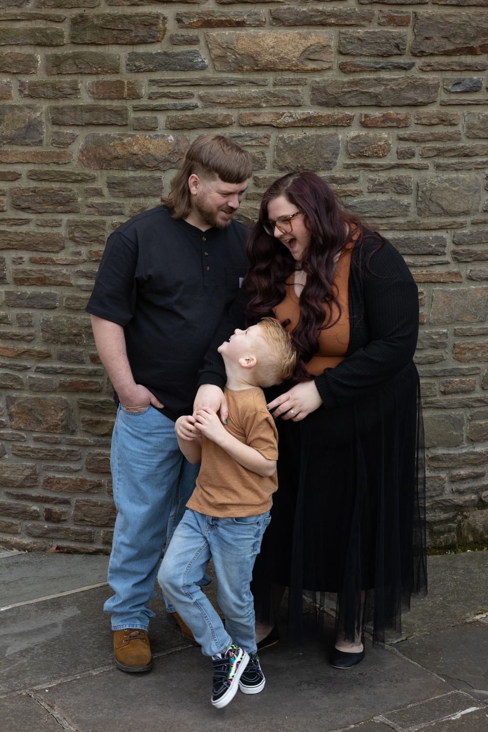 A family shares a playful moment against a stone wall backdrop.