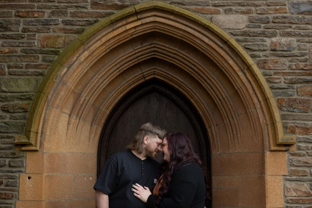 A couple shares an intimate moment under a stone archway entrance of a historic building.