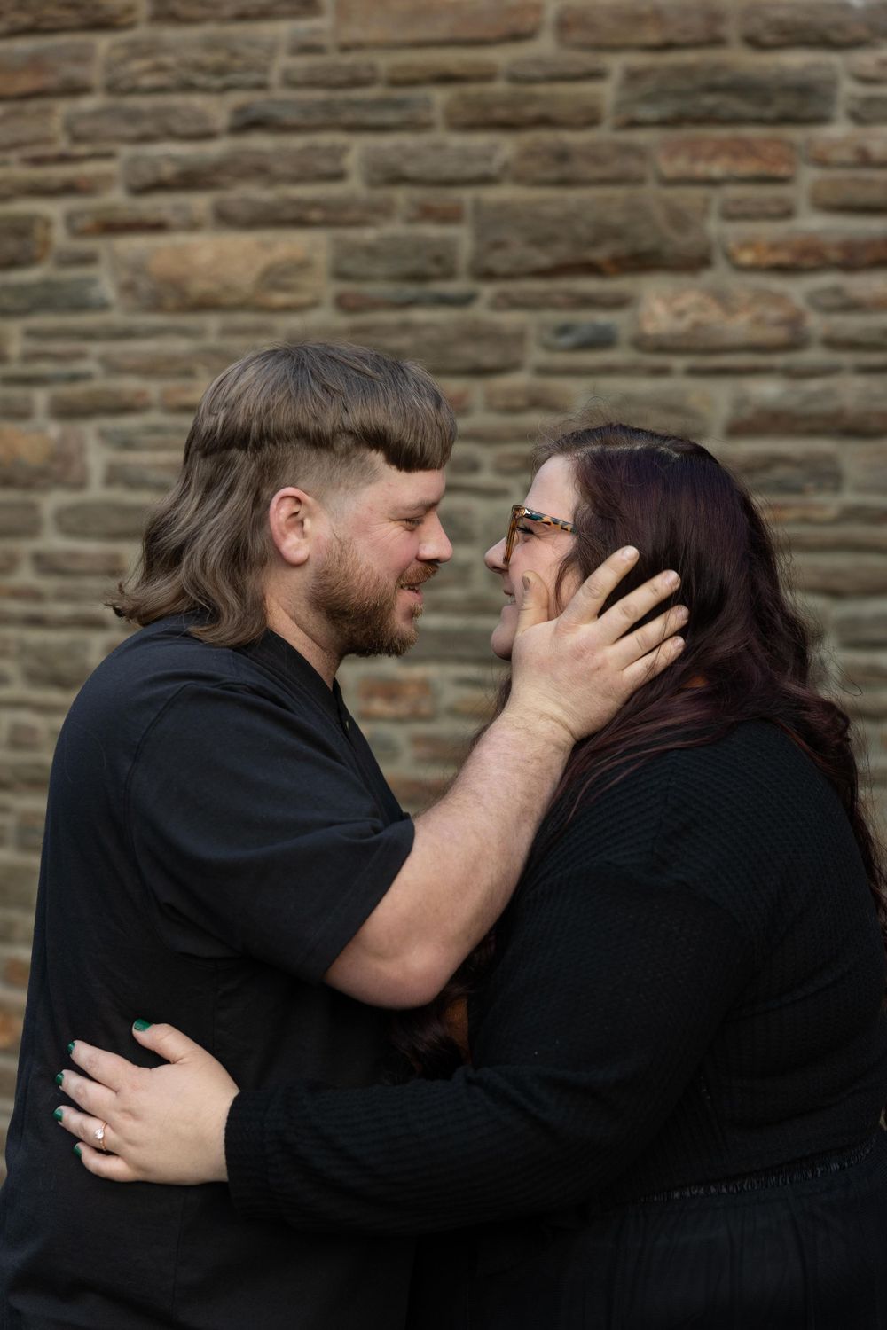 A tender embrace captured against a rustic stone wall backdrop.