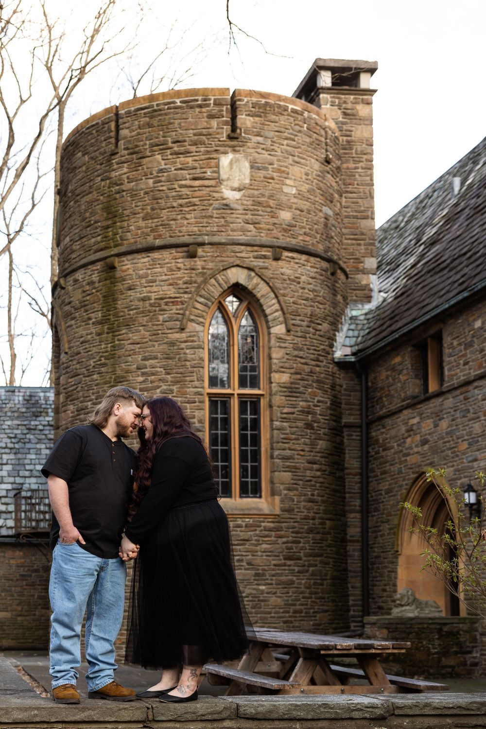 A couple shares a moment outside a circular stone tower with gothic windows.