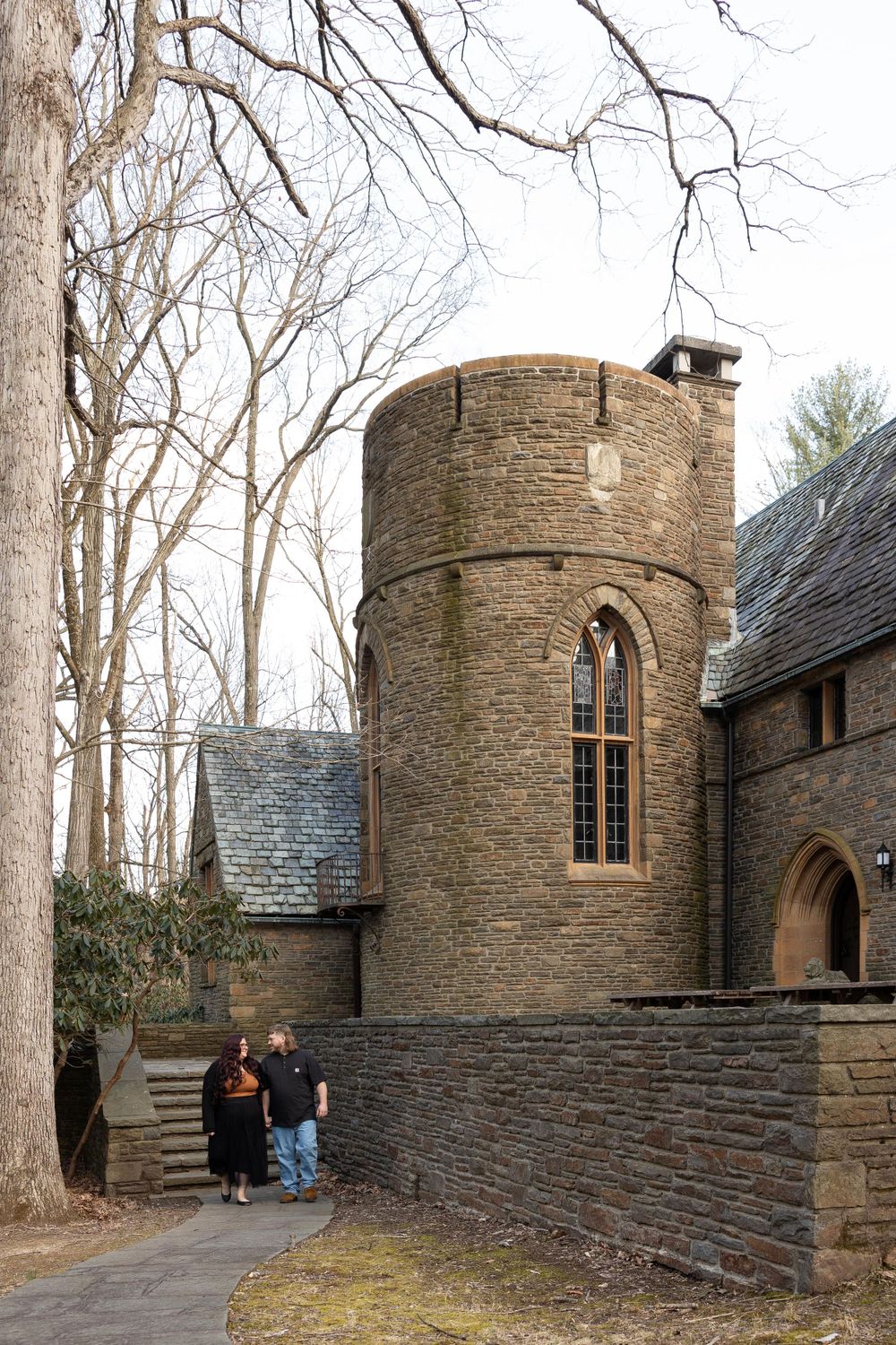 Gothic stone tower with arched windows and surrounding bare trees in winter.