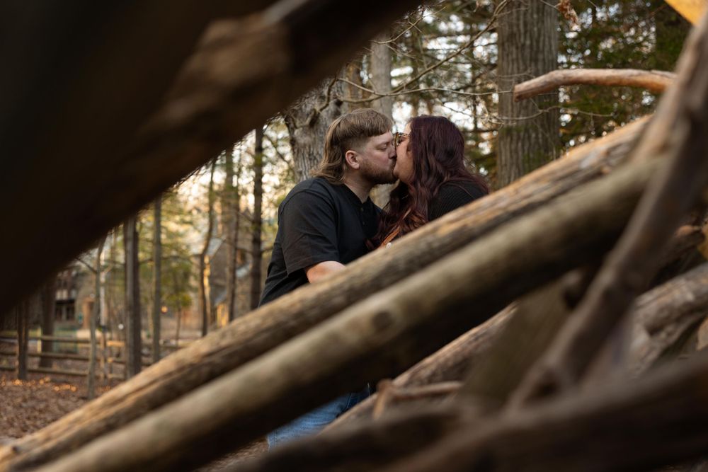 A romantic moment captured through fallen branches in a forest setting.