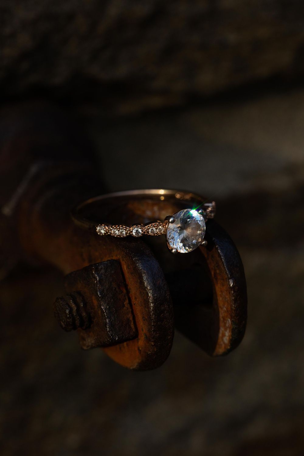 An engagement ring with gemstones photographed on rustic metal machinery.