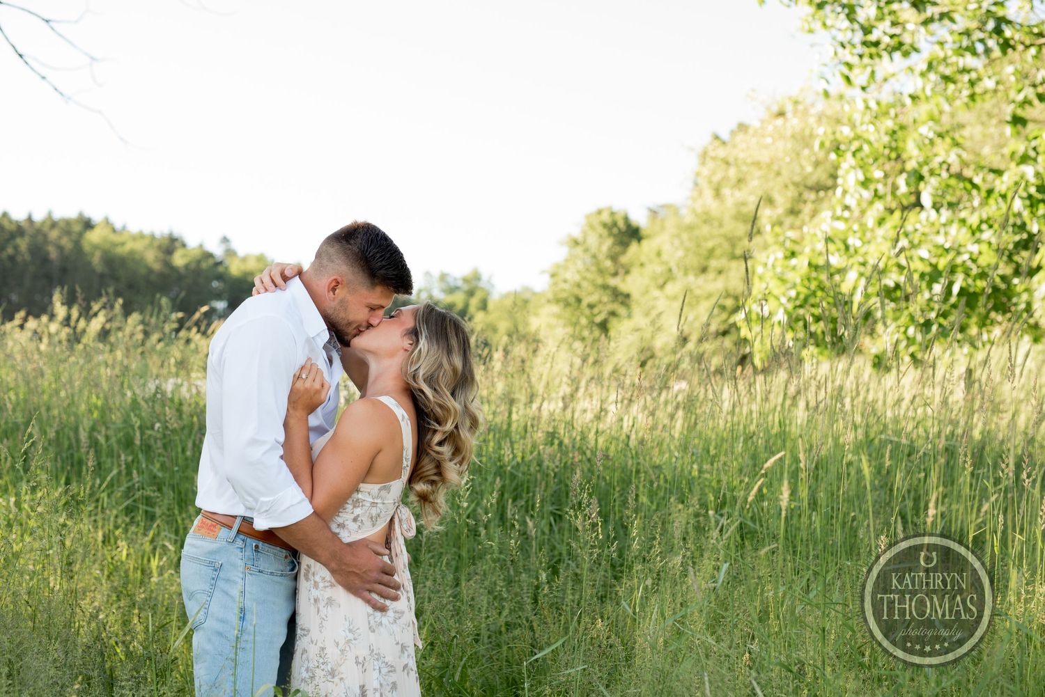 A romantic couple shares an intimate moment in a sunlit field with tall grass.