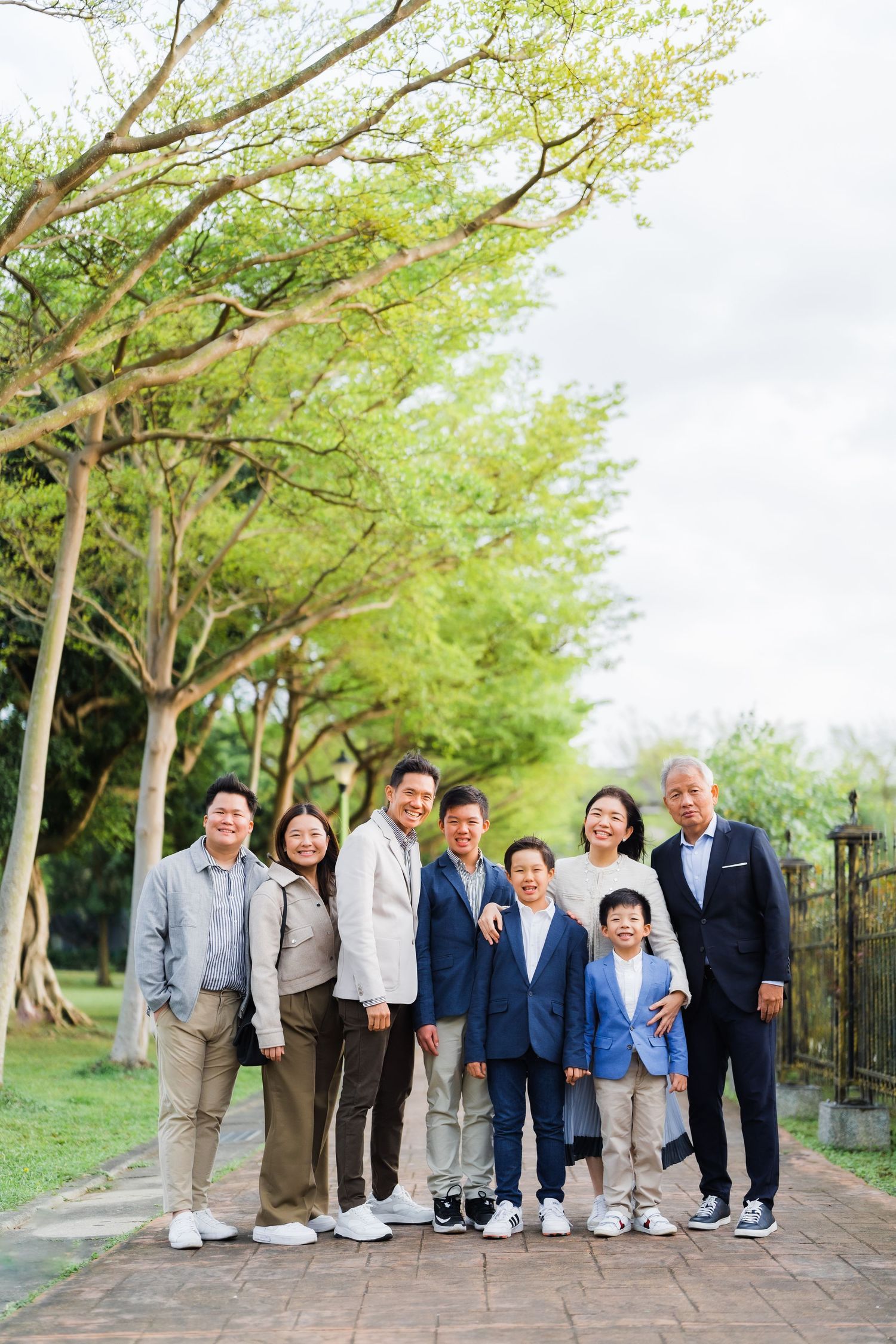 Multi-generational family portrait outdoors with trees in the background.